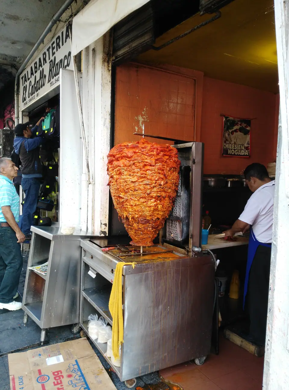 Un trompo de tacos al pastor girando junto a un taquero, en una taquería